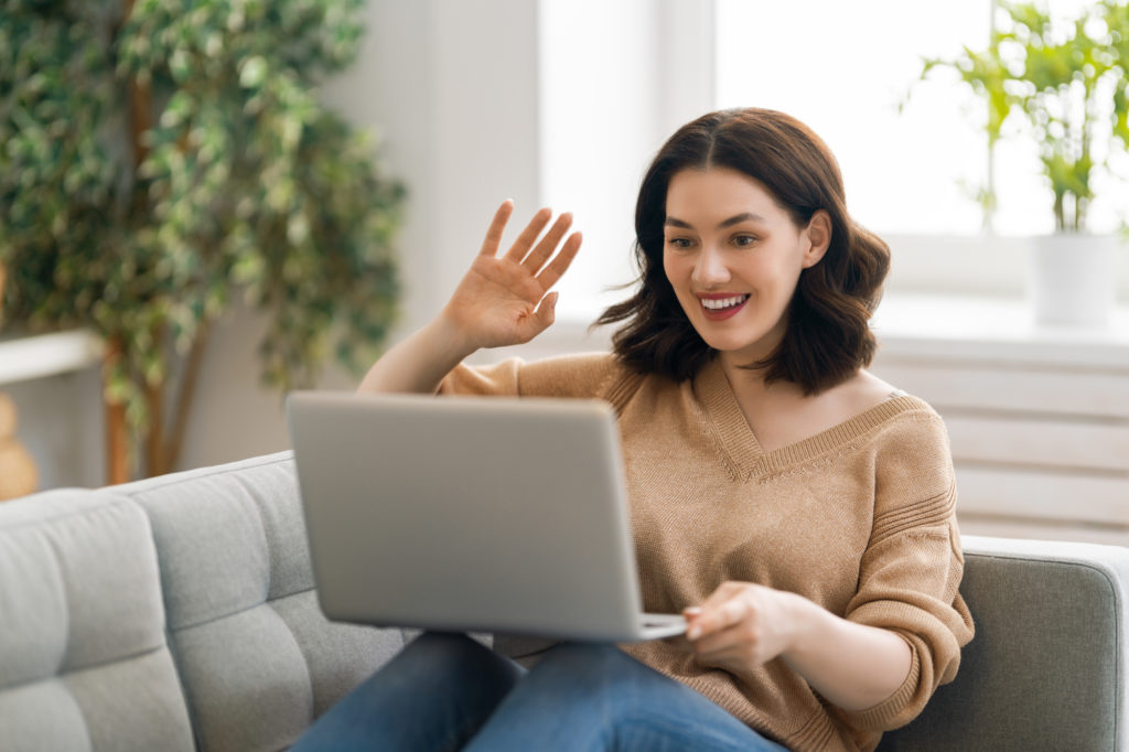 young brunette woman waves hello to her loved ones via video call